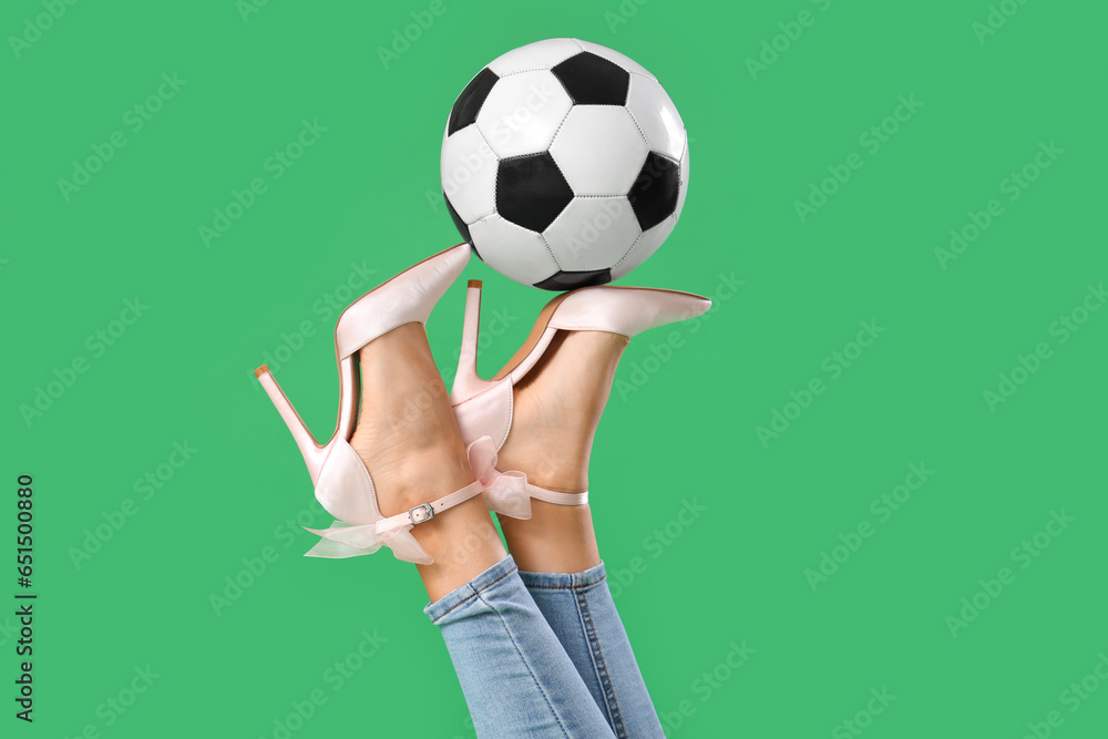 Legs of young woman wearing high heels with soccer ball on green background