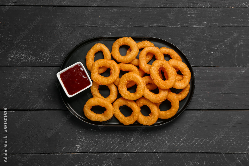 Plate with fried breaded onion rings and ketchup on black wooden background