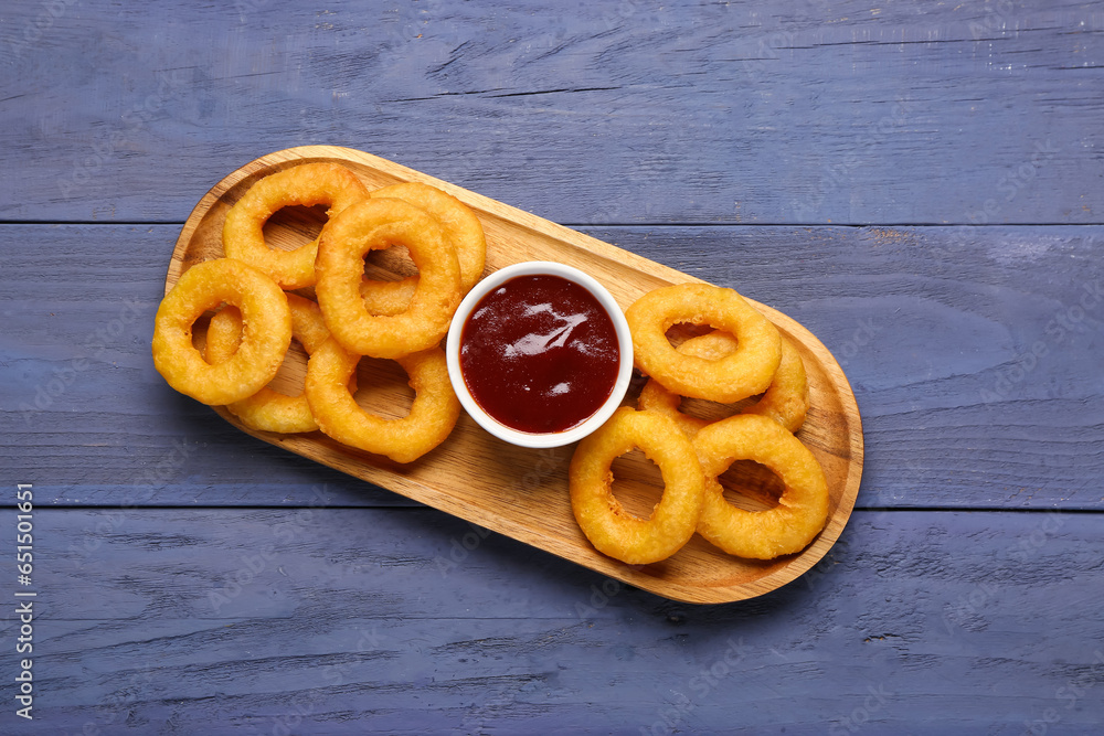 Board with fried breaded onion rings and ketchup on blue wooden background