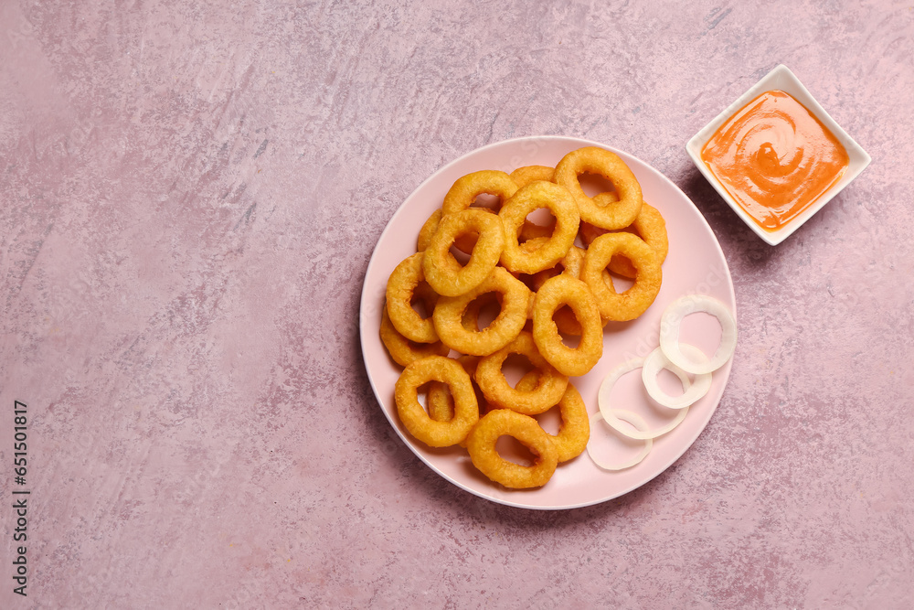 Plate with fried breaded onion rings and sauce on pink background