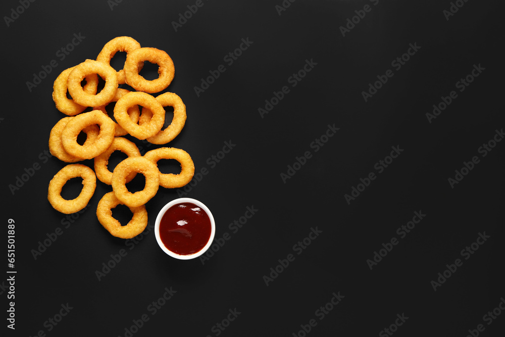 Fried breaded onion rings with ketchup on black background