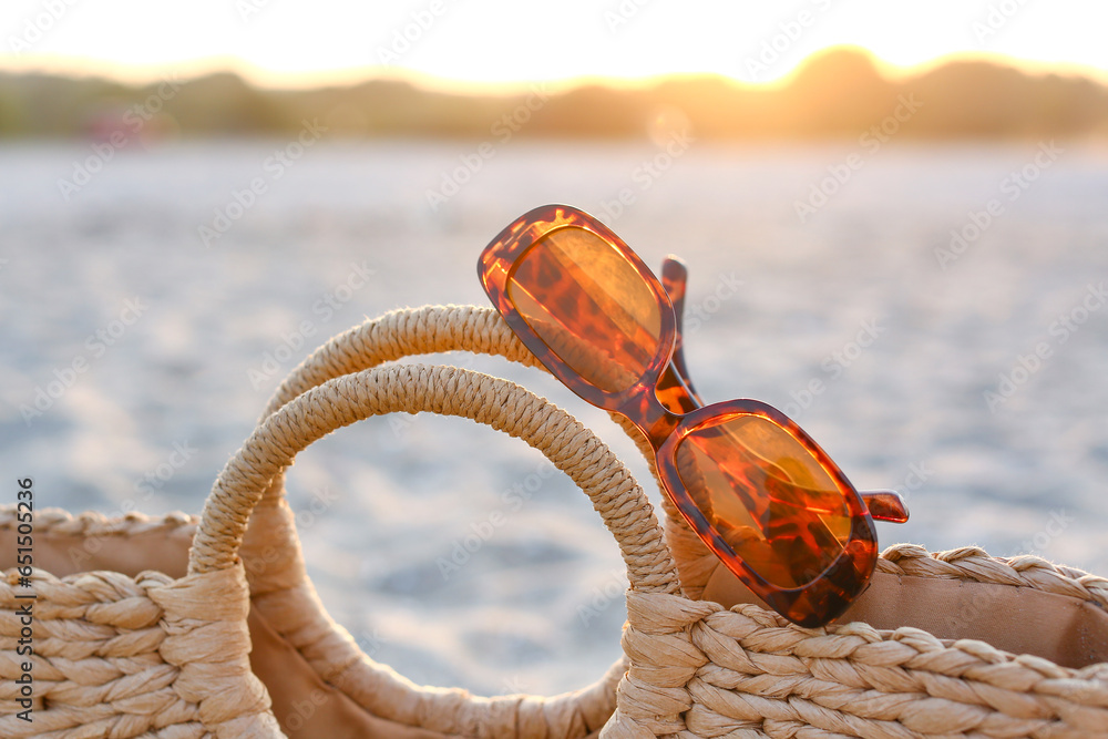 Stylish sunglasses with straw bag, closeup