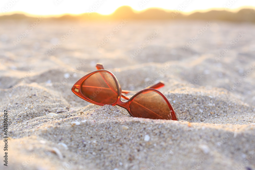 Stylish sunglasses on sandy background