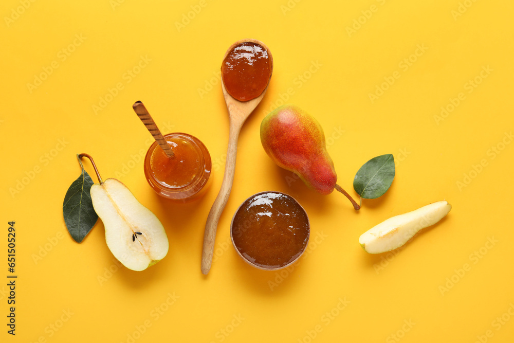 Glass jar and wooden bowl of tasty pear jam with wooden spoons on orange background