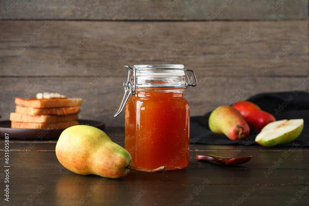 Glass jar of tasty pear jam on wooden background