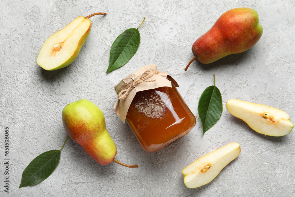 Glass jar of tasty pear jam with leaves on grey background