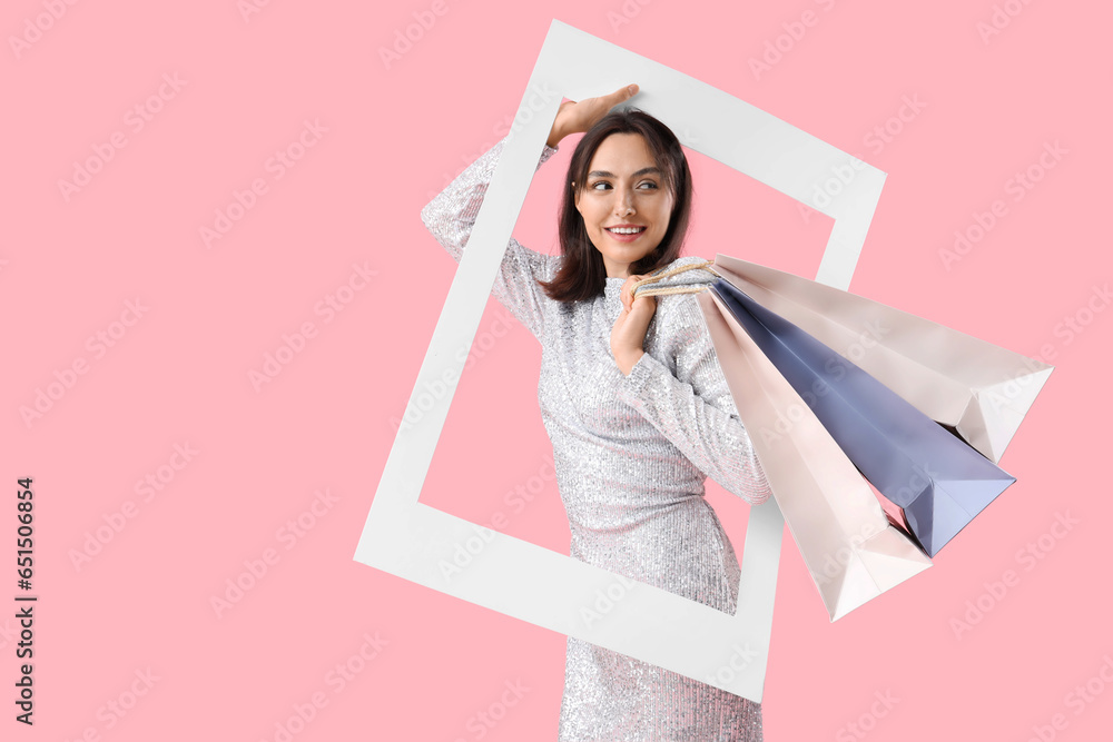 Beautiful young woman with shopping bags and frame on pink background