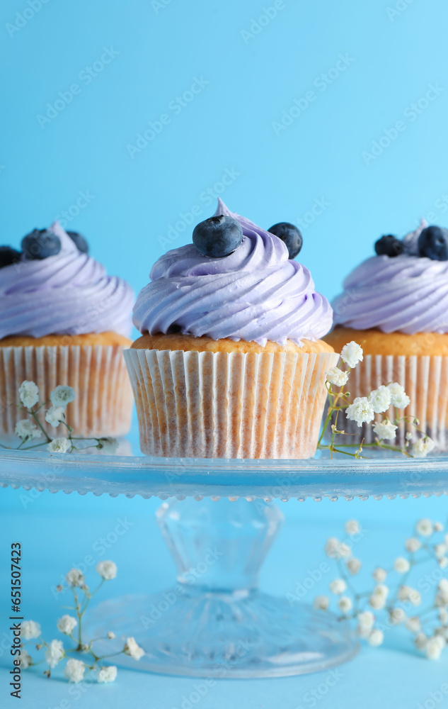 Stand of tasty cupcakes with blueberries on blue background