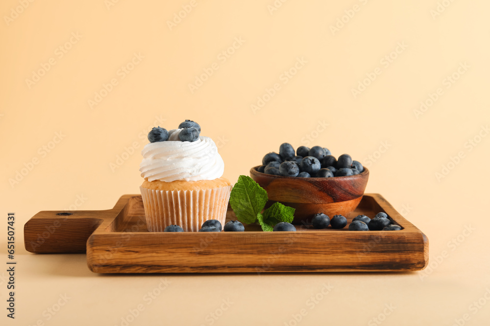 Wooden board of tasty cupcake with blueberries on yellow background