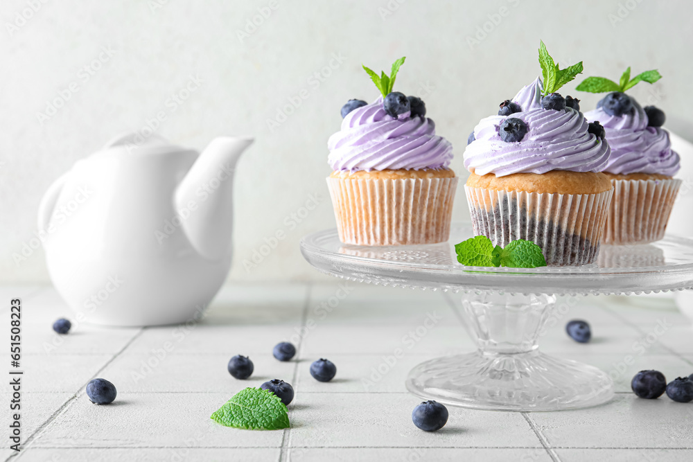 Glass stand of delicious cupcakes with blueberries and mint on white tile table