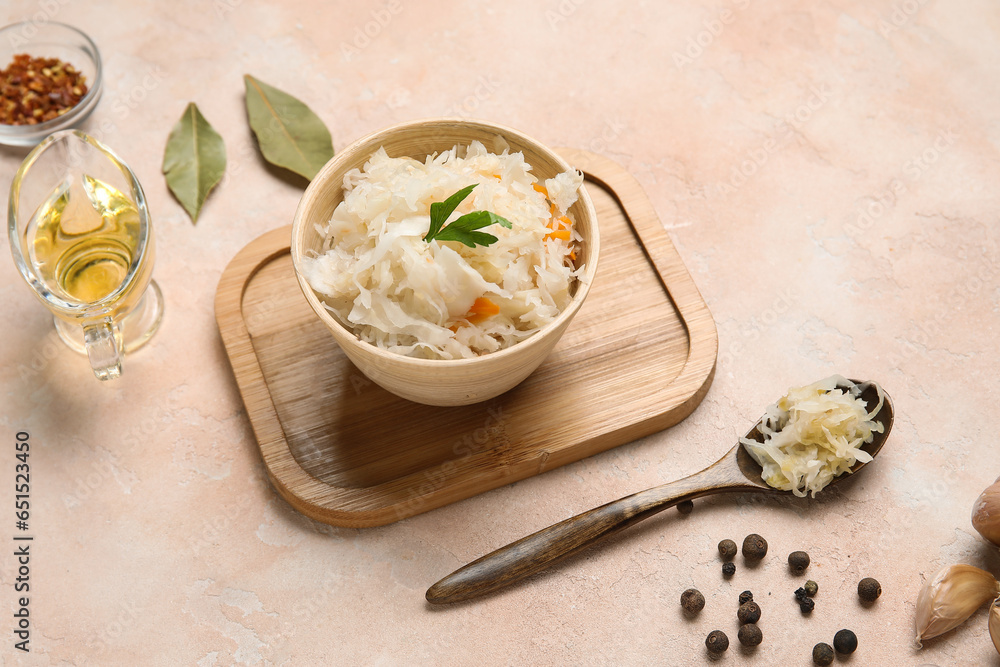 Bowl and spoon of delicious sauerkraut with different spices on pink background