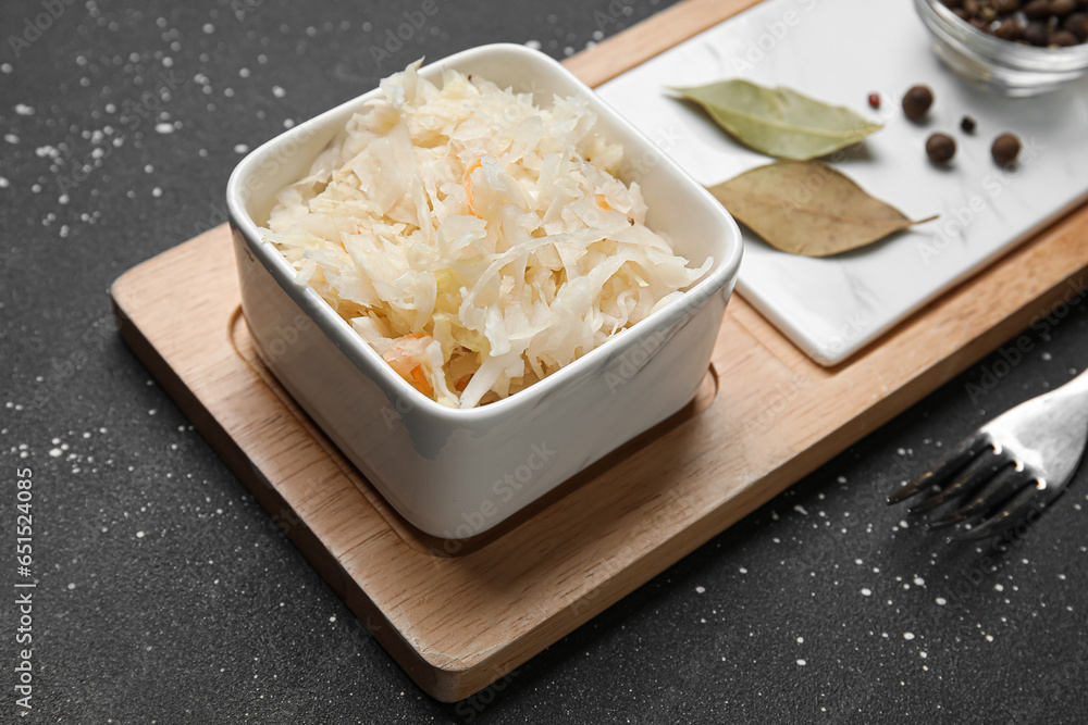 Bowl of delicious sauerkraut with bay leaves and peppercorn on black background