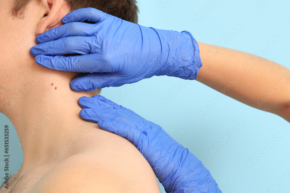 Dermatologist examining moles on young mans neck against blue background, closeup