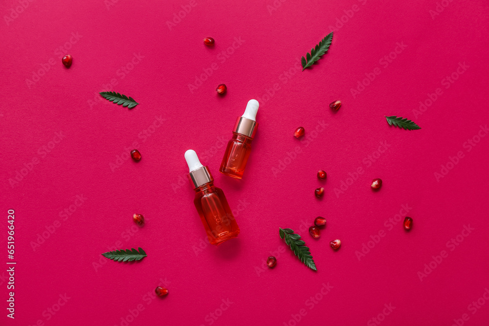 Composition with bottles of essential oil, pomegranate seeds and plant leaves on color background