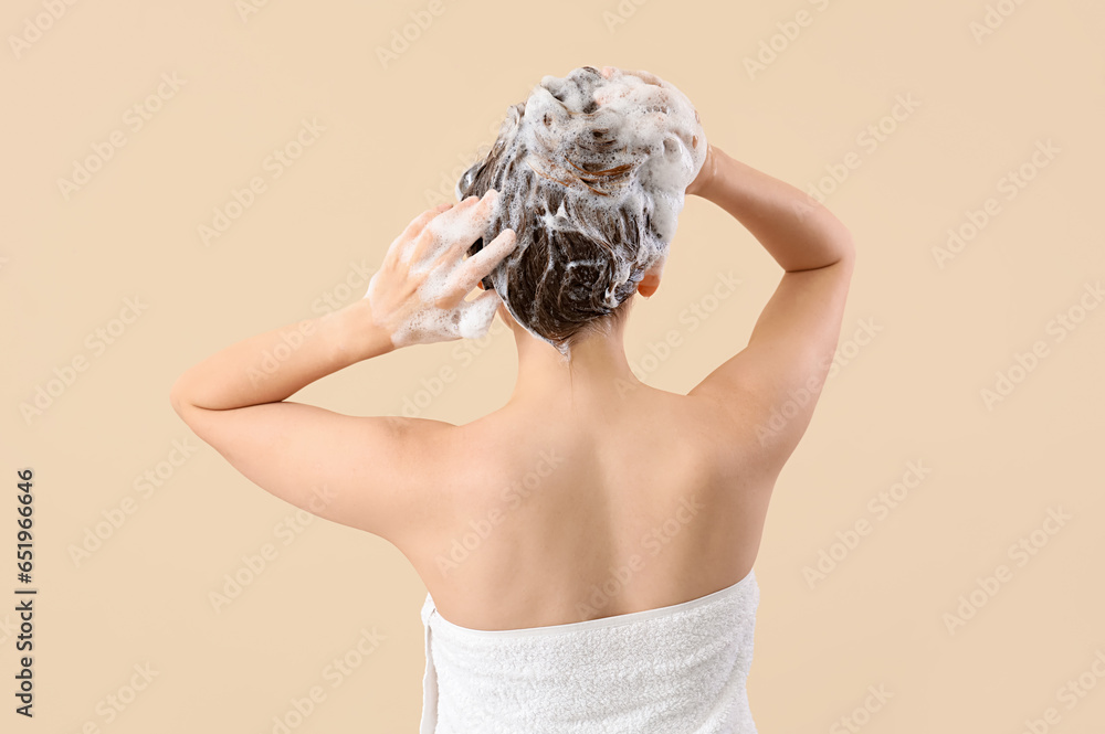 Young woman washing hair on beige background, back view