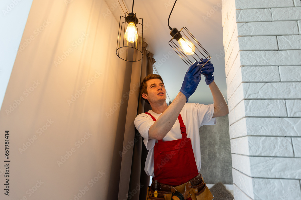 Worker installing lamp on stretch ceiling indoors.