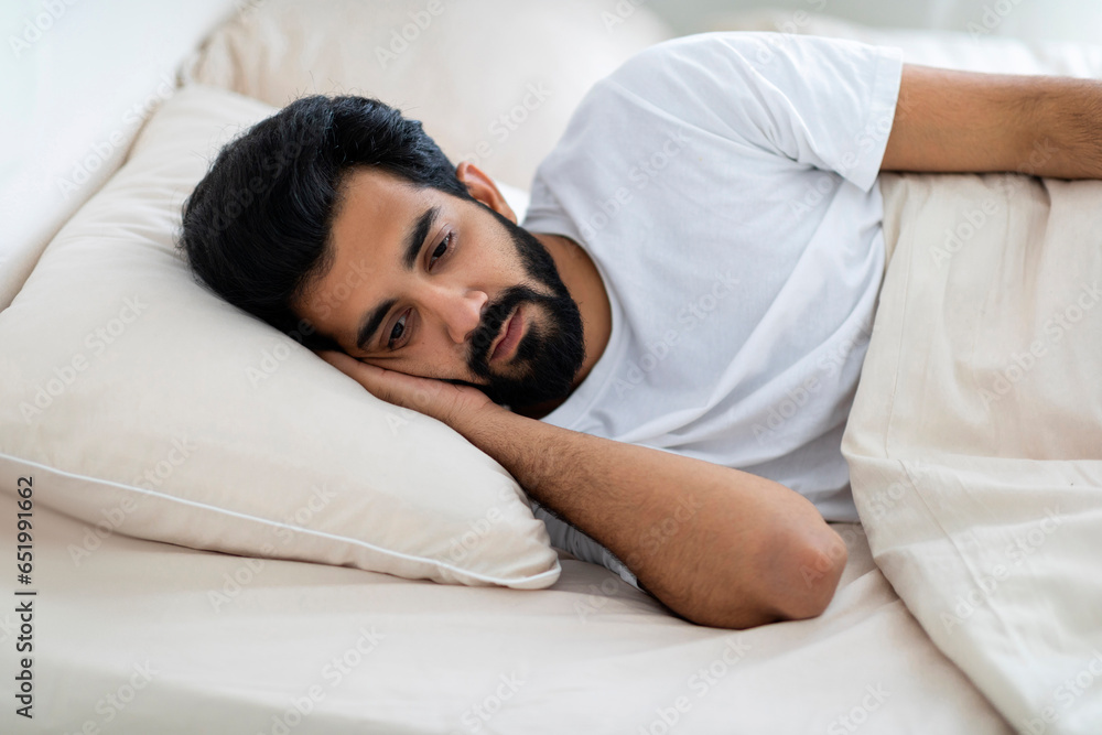 Portrait Of Sad Young Indian Man Lying In Bed With Eyes Open