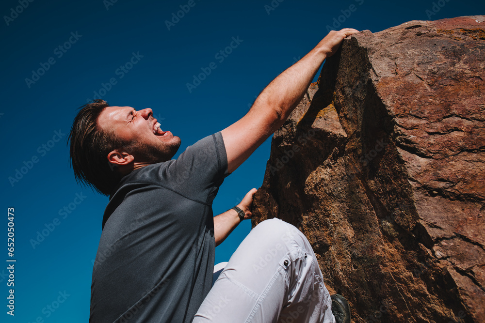 Young man tourist surviving falling from high mountain and trying to climb up