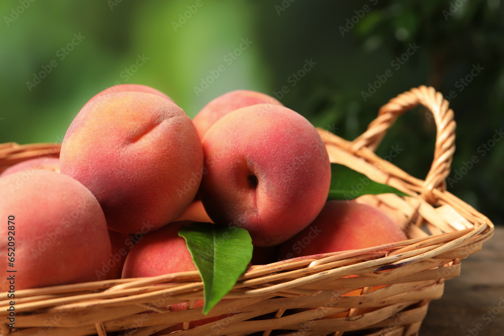 Fresh peaches and leaves in basket on table against blurred green background, closeup