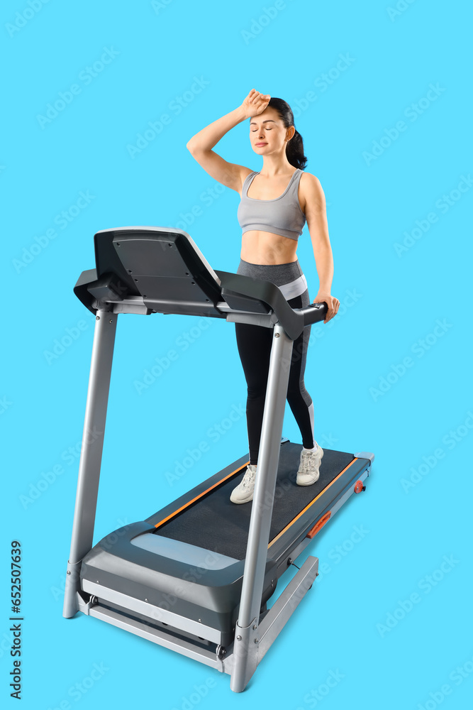 Beautiful woman training on treadmill against blue background