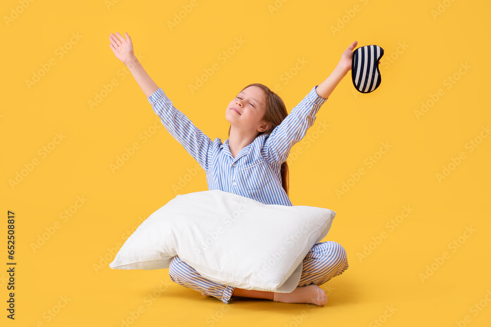 Little girl with pillow and sleep mask on yellow background