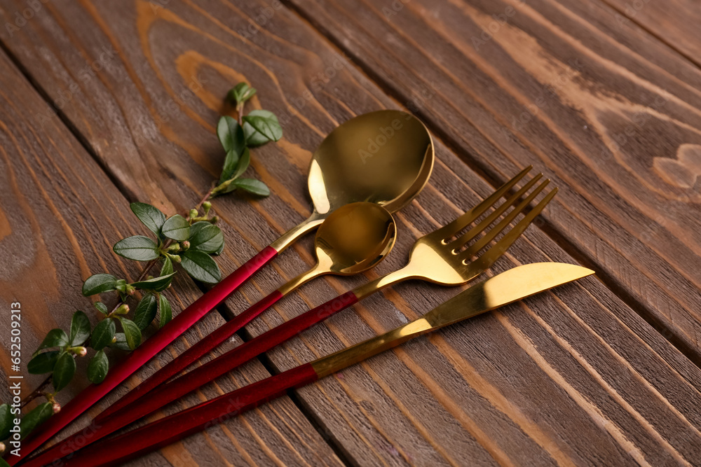 Golden cutlery with red handle and cotoneaster twig on wooden background