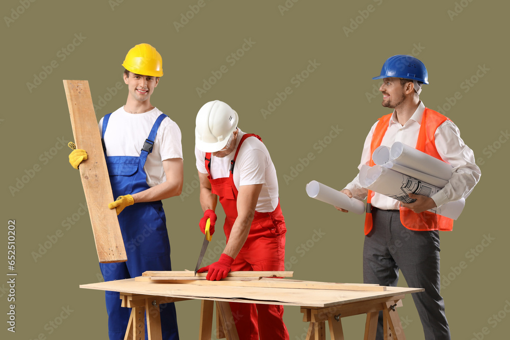 Team of male builders with wooden planks and house plans on green background