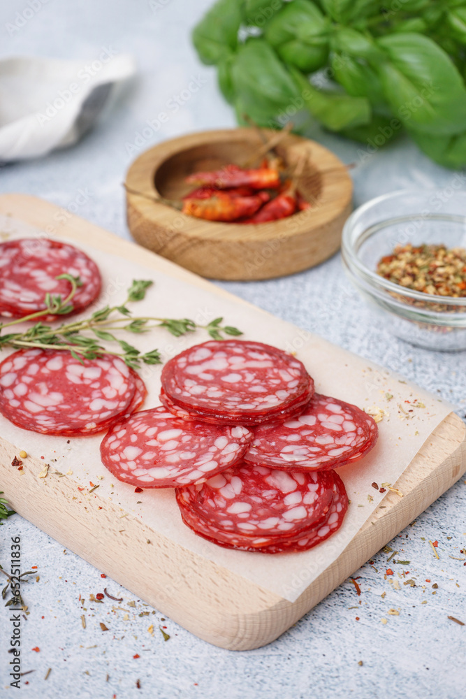 Wooden board with slices of tasty salami on light background