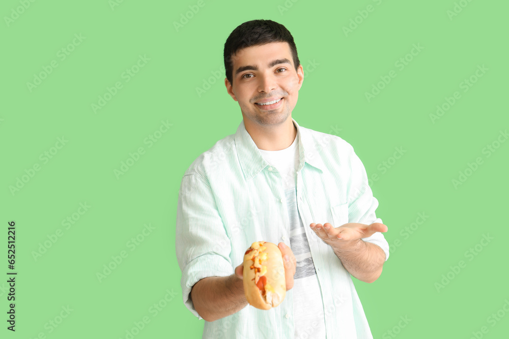 Happy young man with tasty hot dog on green background