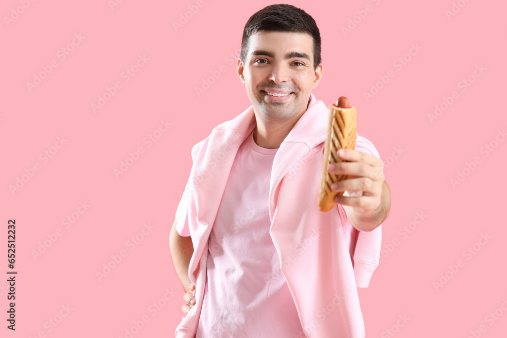 Happy young man with tasty french hot dog on pink background