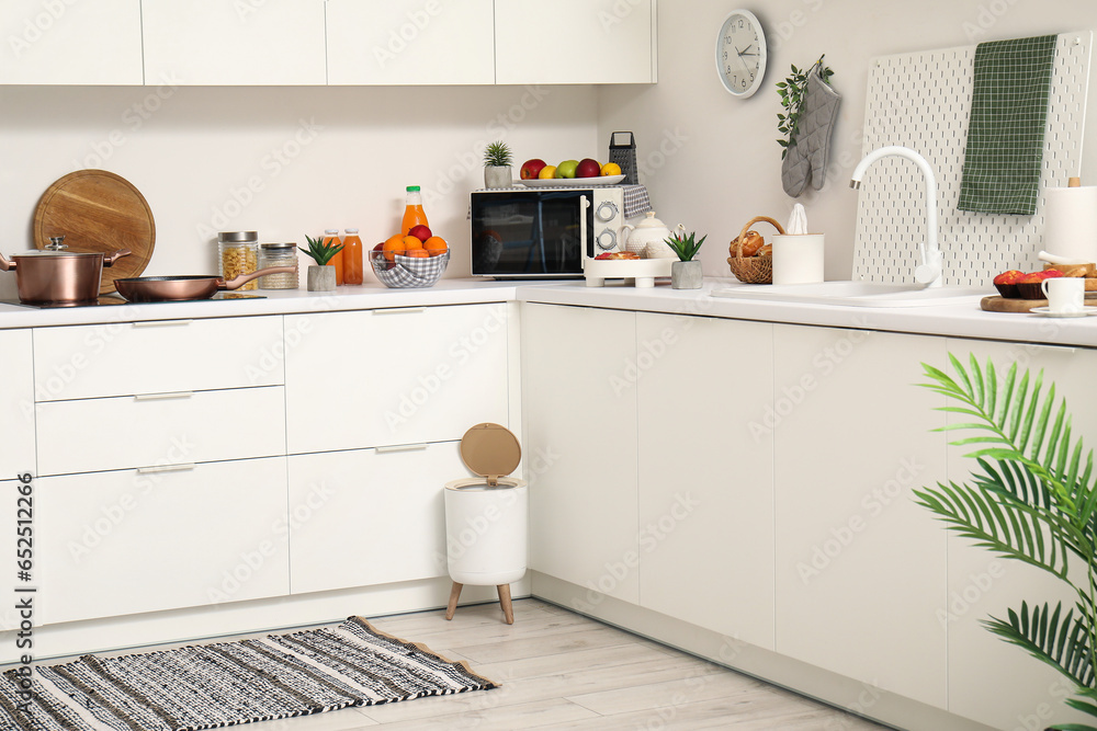 Interior of modern kitchen with stylish rug, trash bin and white counters