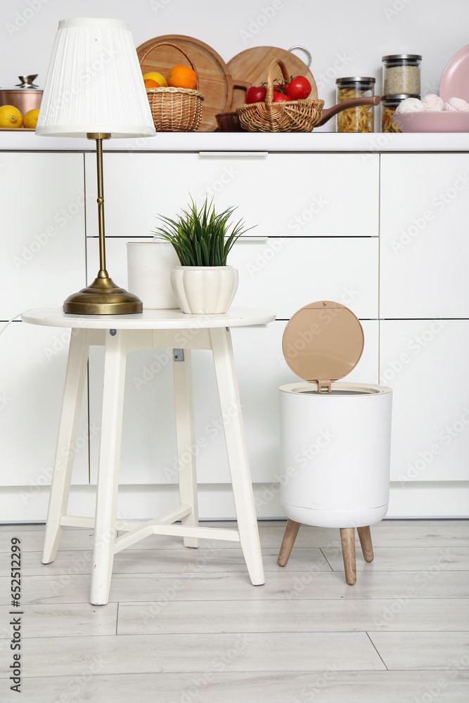 Trash bin and small table with lamp on floor in modern kitchen