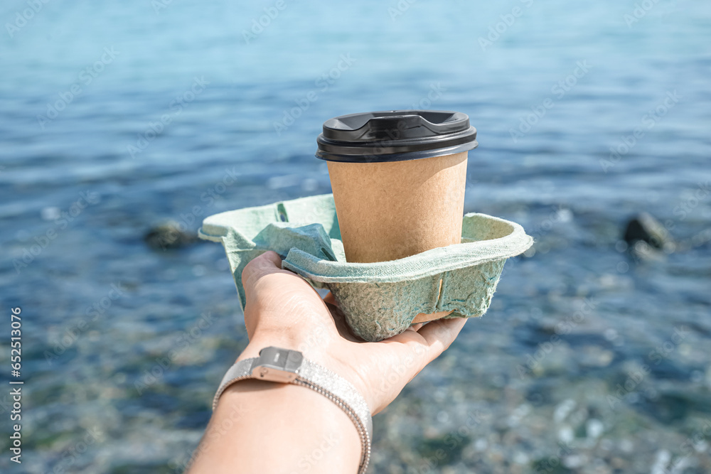 Woman holding takeaway cup of hot coffee on beach