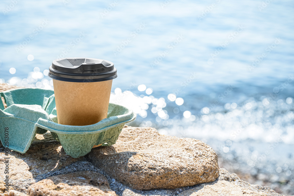 Holder with takeaway cup of hot coffee on beach