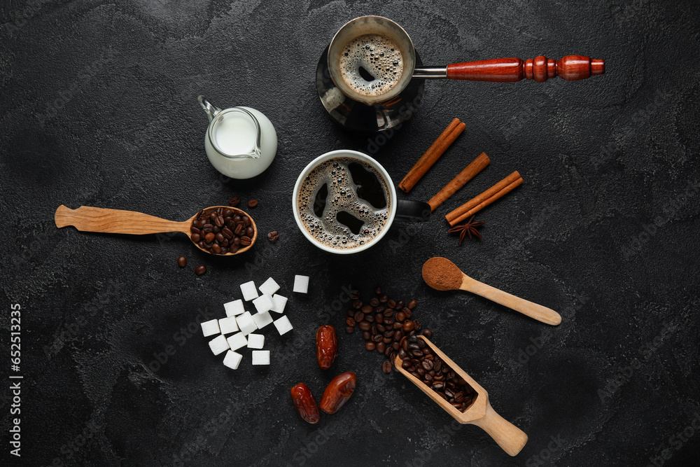 Cezve with cup of tasty coffee, beans, powder, sugar, cinnamon, dried dates and milk on black background