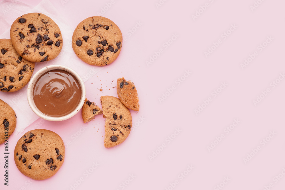 Tasty cookies with chocolate chips and bowl of sauce on pink background