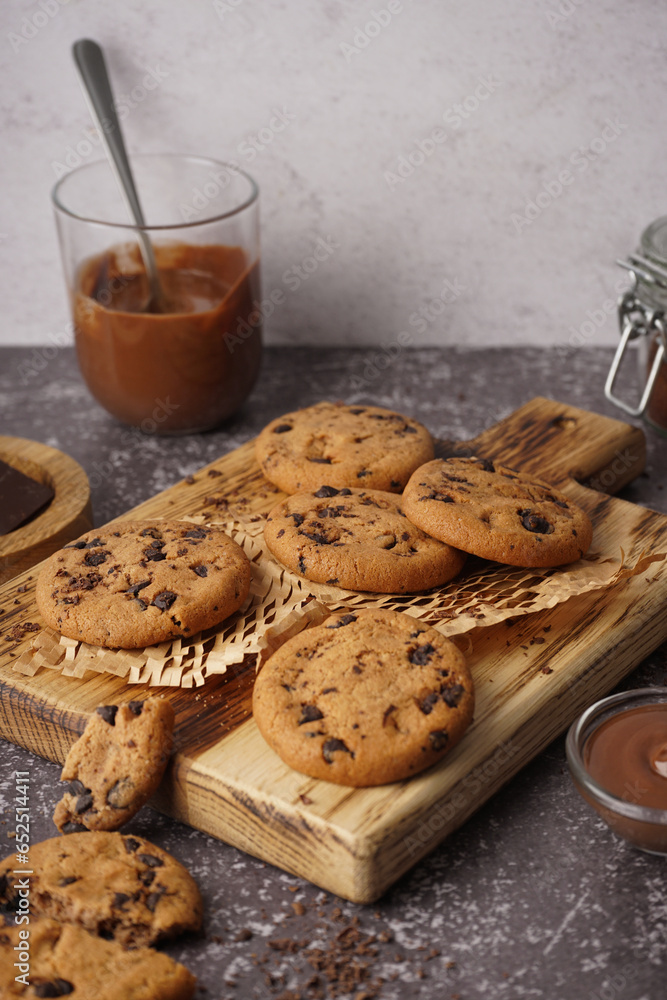 Wooden board of tasty cookies with chocolate chips on table