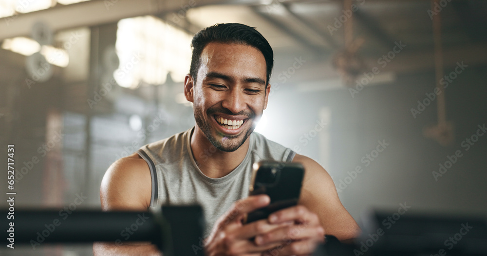 Happy asian man, phone and fitness on break in social media, communication or networking at gym. Active male person smile for online texting or chatting on mobile smartphone app at indoor health club