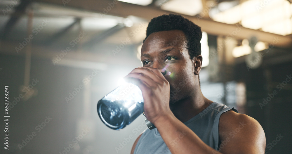 Black man at gym, water bottle and relax to hydrate in muscle development, strong body and fitness. Commitment, motivation and bodybuilder with drink in workout challenge for health and wellness.