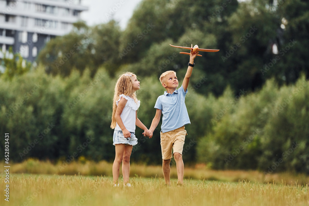 Boy and girl are playing with toy plane on the green field