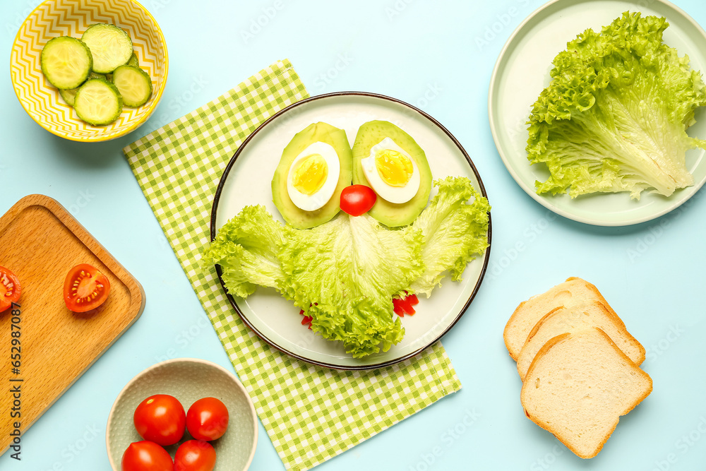 Plate with funny breakfast in shape of owl, vegetables and bread on blue background