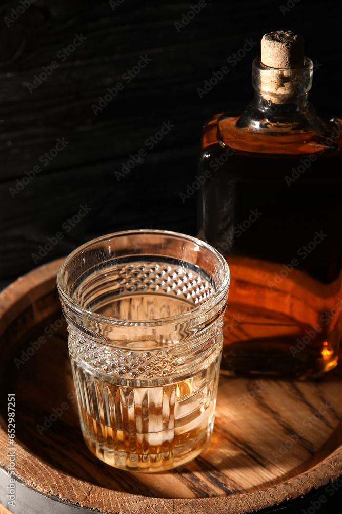 Oak barrel with bottle and glass of cold whiskey on dark wooden background