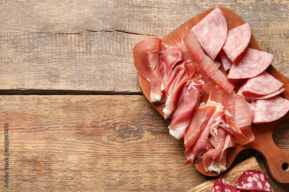 Board with assortment of tasty deli meats on wooden background