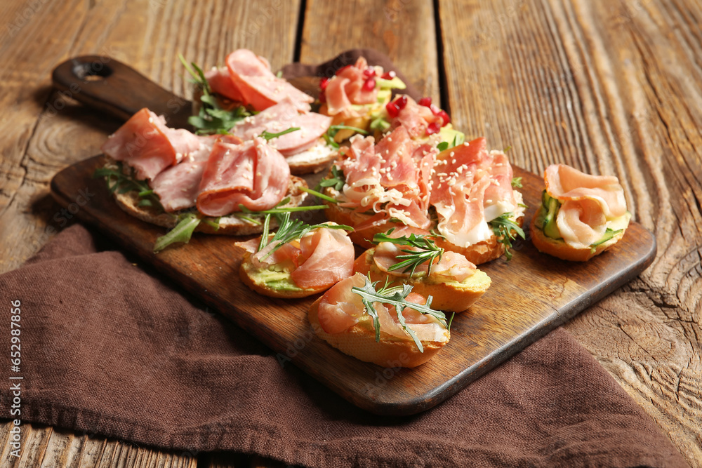 Board of tasty bruschettas with ham on wooden background