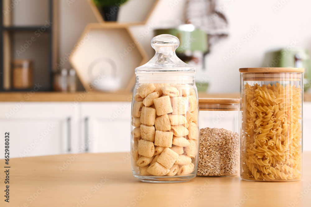 Jars with different food on wooden table in kitchen