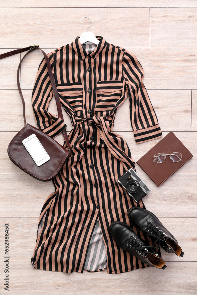 Stylish dress with accessories, photo camera, mobile phone and book on light wooden floor