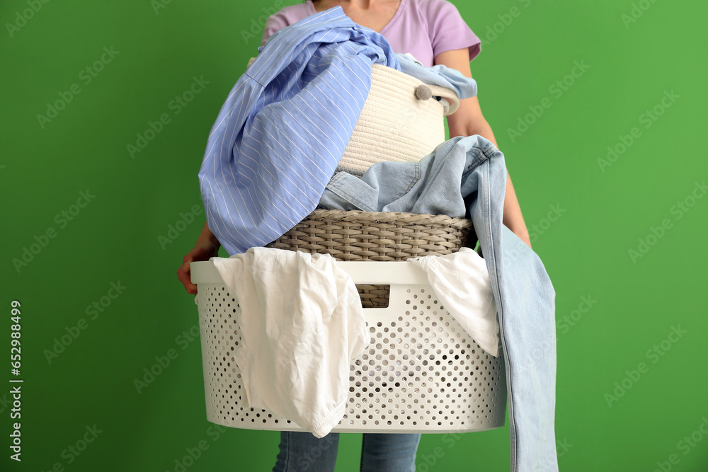 Housewife with baskets of dirty clothes on green background