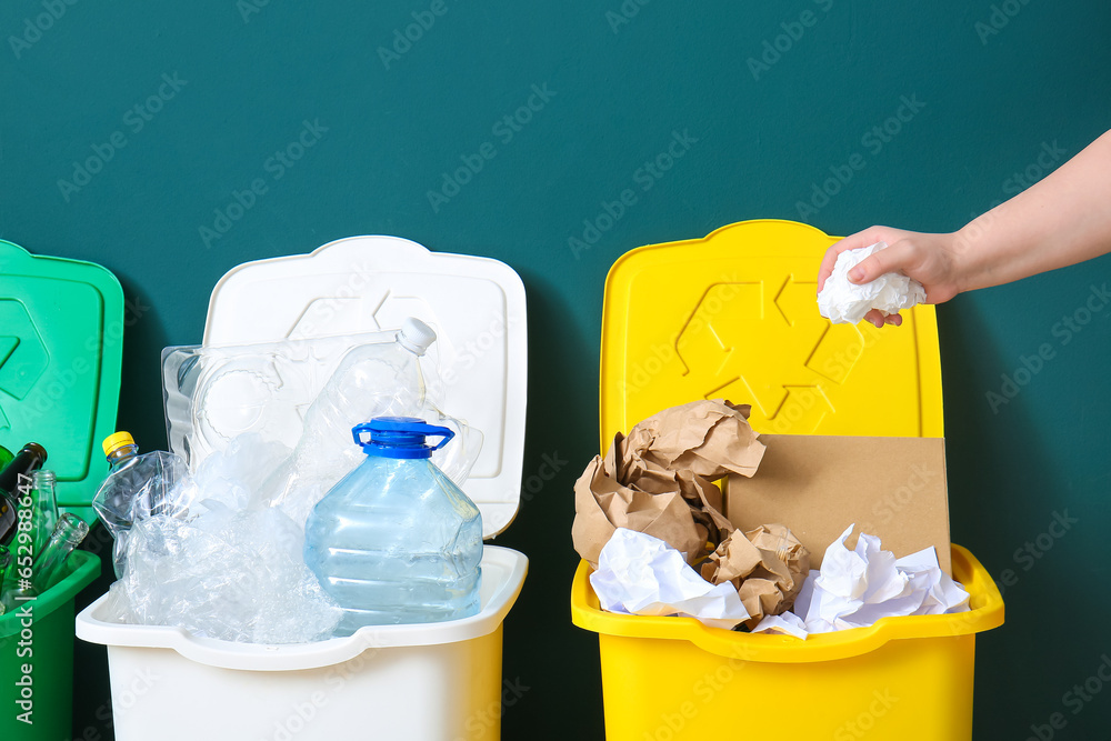 Woman throwing garbage into trash bin near green wall. Recycling concept