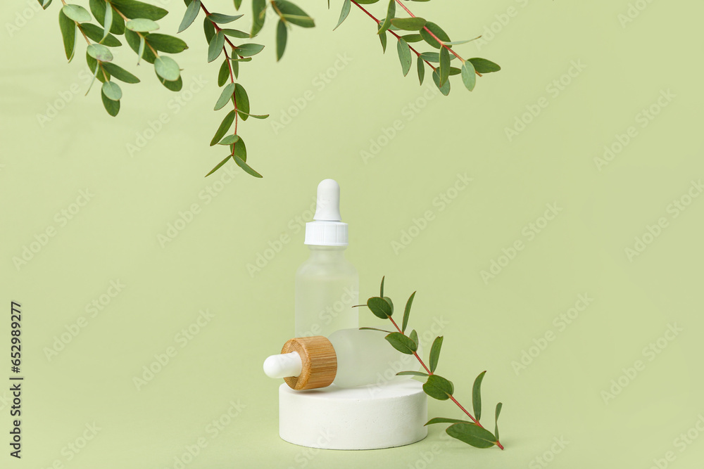 Bottles of cosmetic oil with eucalyptus twigs and stand on light green background