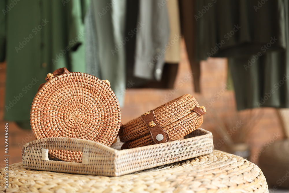 Tray with stylish wicker bags on pouf in boutique, closeup